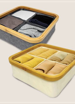 Two bamboo storage boxes with divided compartments containing folded clothes on a light background