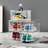 Clear acrylic shoe display boxes with variously colored sneakers on a gray floor.